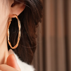 Close-up of vintage golden hoop earring with twisted texture on a soft warm background