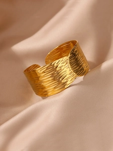 Vue détaillée du bracelet en acier plaqué or 18K avec texture ondulée sur fond de soie