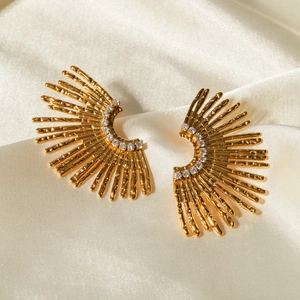 Nahaufnahme goldener Ohrringe im Sonnenstrahl-Design mit Schmucksteinen auf hellem Satin