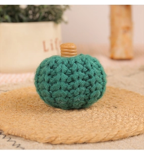 Close-up of a handmade green knitted pumpkin decoration on a rustic woven mat