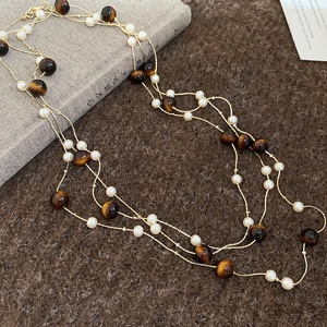 Détail d'un collier doré multicouche avec pierres œil de tigre et perles sur peluche