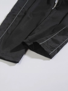 Close-up of black woven trousers showing stitching and gray reflective strip details