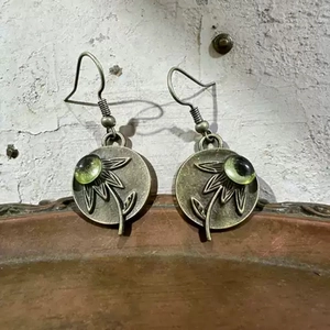 Detalle de pendientes de bronce vintage con relieve de girasol y gema verde esmeralda