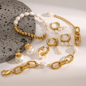Elegant gold stainless steel jewelry set with pearls on a textured stone display