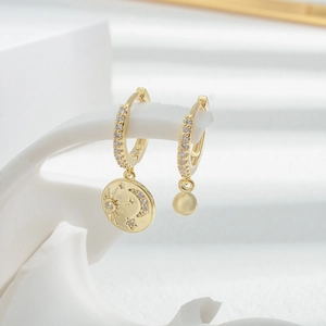 Asymmetric gold star and moon hoop earrings set with zircon stones on white background