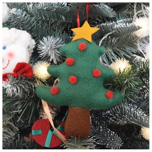 Green felt Christmas tree ornament with red pom-poms hanging on a lit Xmas tree
