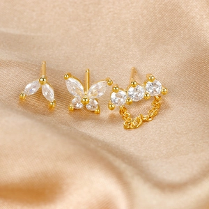 Macro detail of gold butterfly and leaf stud earrings with chains on champagne silk