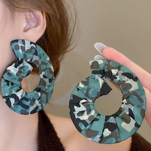 Close-up of oversized hollow round earrings wrapped in blue-green camo print fabric