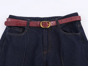 Gros plan sur denim bleu foncé avec ceinture croco bordeaux et boucle dorée vintage