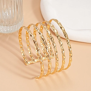 Detailed view of multilayer gold cuff bracelet with hammered wavy texture and glossy finish