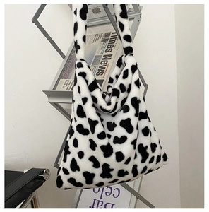 Detail view of cow print plush tote bag hanging on a silver metal magazine rack