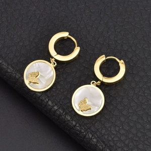 Close-up of golden round earrings with white shell inlay and matte butterfly detail