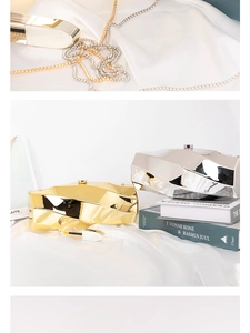 Detail of geometric metallic mirror clutch bag resting on silk fabric and art books