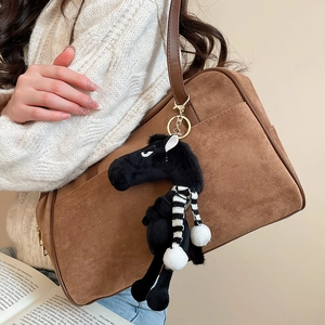 Detail view of a black plush horse charm with a striped scarf on a brown suede bag