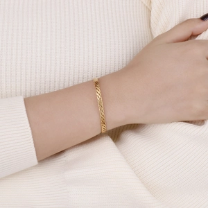 Gros plan d'un bracelet torsadé doré au poignet d'une femme sur fond de tricot blanc cassé