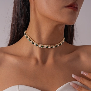 Close-up of gold choker necklace with green square gem and sparkling white crystals