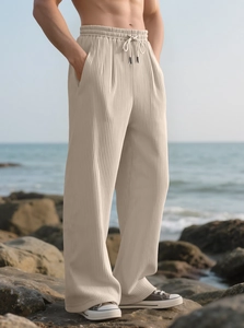Detail of beige vertical pleated wide-leg trousers with drawstring waist on beach rock