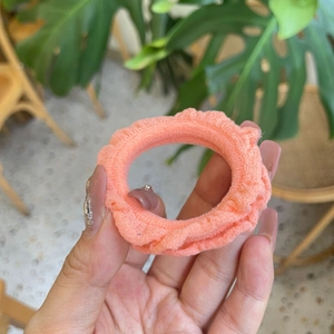 Hand holding a pink ruffled cotton fabric scrunchie in a natural indoor setting