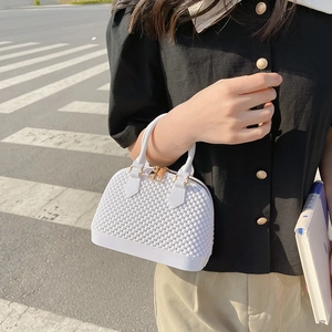 White shell jelly handbag with textured surface and gold hardware on a city street