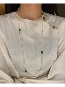 Detail of long pearl necklace with green beads worn on an elegant white silk garment