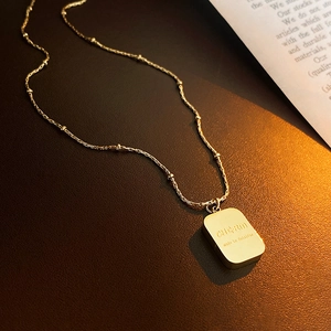 Macro shot of gold square pendant necklace with CHARM engraving on brown texture