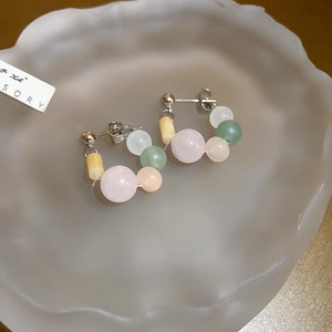 Macro shot of silver stud earrings with pastel pink and green macaron beads on glass tray