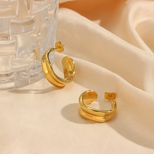 Macro shot of gold-plated irregular curved hoop earrings on beige silk fabric