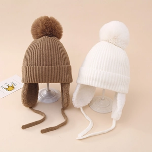 Détail de bonnets tricotés à oreillettes en marron et blanc avec pompons en fausse fourrure