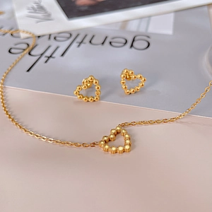 Détail de l'ensemble collier et boucles d'oreilles cœur dorés à texture perlée
