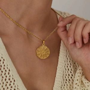 Detail of a gold sun totem pendant on a twisted chain necklace worn by a model