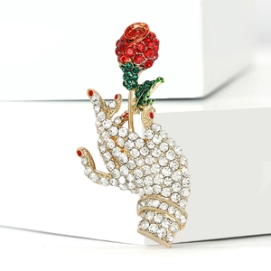 Artistic hand holding rose brooch with red and green rhinestones on gold base