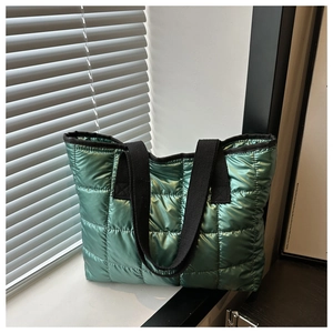 Detail of green metallic quilted tote bag with square pattern and black straps on windowsill