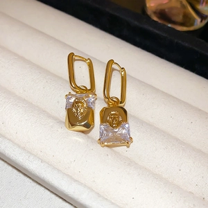 Macro shot of gold-plated lion head earrings with rectangular zircon on white jewelry box