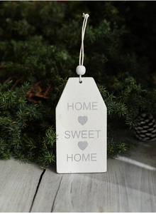 Close-up of wooden Home Sweet Home hanging ornament with white beads on pine branches