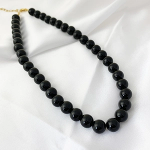 Detailed close-up of black onyx beaded necklace with gold clasp on white silk
