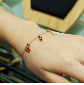 Detailed close-up of 18K gold-plated bracelet with red gemstone and star charms