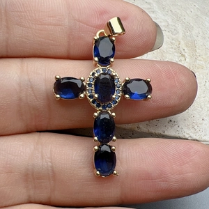 Detailed macro view of a gold cross pendant featuring deep blue zircon stones on a finger