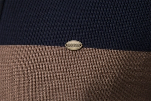 Close-up of color-block knit sweater texture with a metallic brand emblem on the fabric