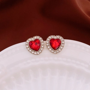 Gros plan de boucles d'oreilles cœur rouge avec base dorée et cristaux sur une assiette
