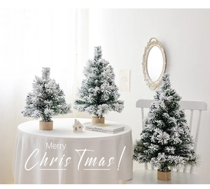 Three flocked mini Christmas trees with snowy needles and natural wood bases on a white table