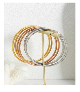 Detailed view of three-color stainless steel bangles hanging on a gold jewelry stand