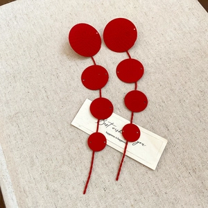 Detail of red tiered disc earrings with spiral texture and bohemian tassel design
