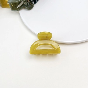 Detail of a translucent mustard yellow jelly texture small hair claw clip in a semi-circle design