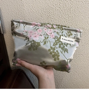 Satin cosmetic bag with pink floral print held by hand against a textured wall