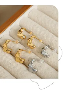 Macro shot of twisted gold and silver C-shaped hoop earrings on a jewelry tray