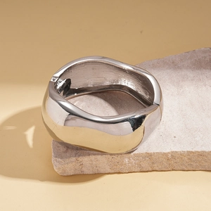 Close-up of a silver wide cuff bracelet with liquid metal design on a natural stone base