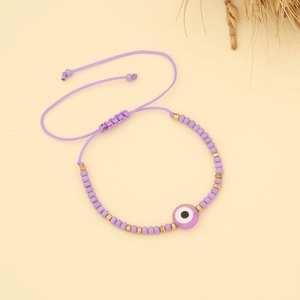 Detail of adjustable purple woven bead bracelet with evil eye charm on yellow surface