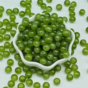 Macro shot of 8mm green glass jade round beads in white ceramic flower bowl for DIY