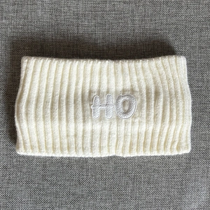 Macro detail of rib-knit cream headband with HO embroidered patch and soft wool texture