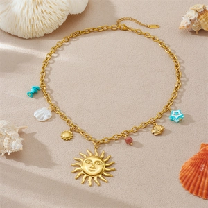 Goldene Edelstahlkette mit Sonnenanhänger, Seestern und Muschel auf sandigem Strand